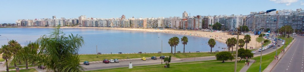 A panoramic view of Playa Pocitos with the blue Rio de la Plata lapping at the beach along the city's edge.